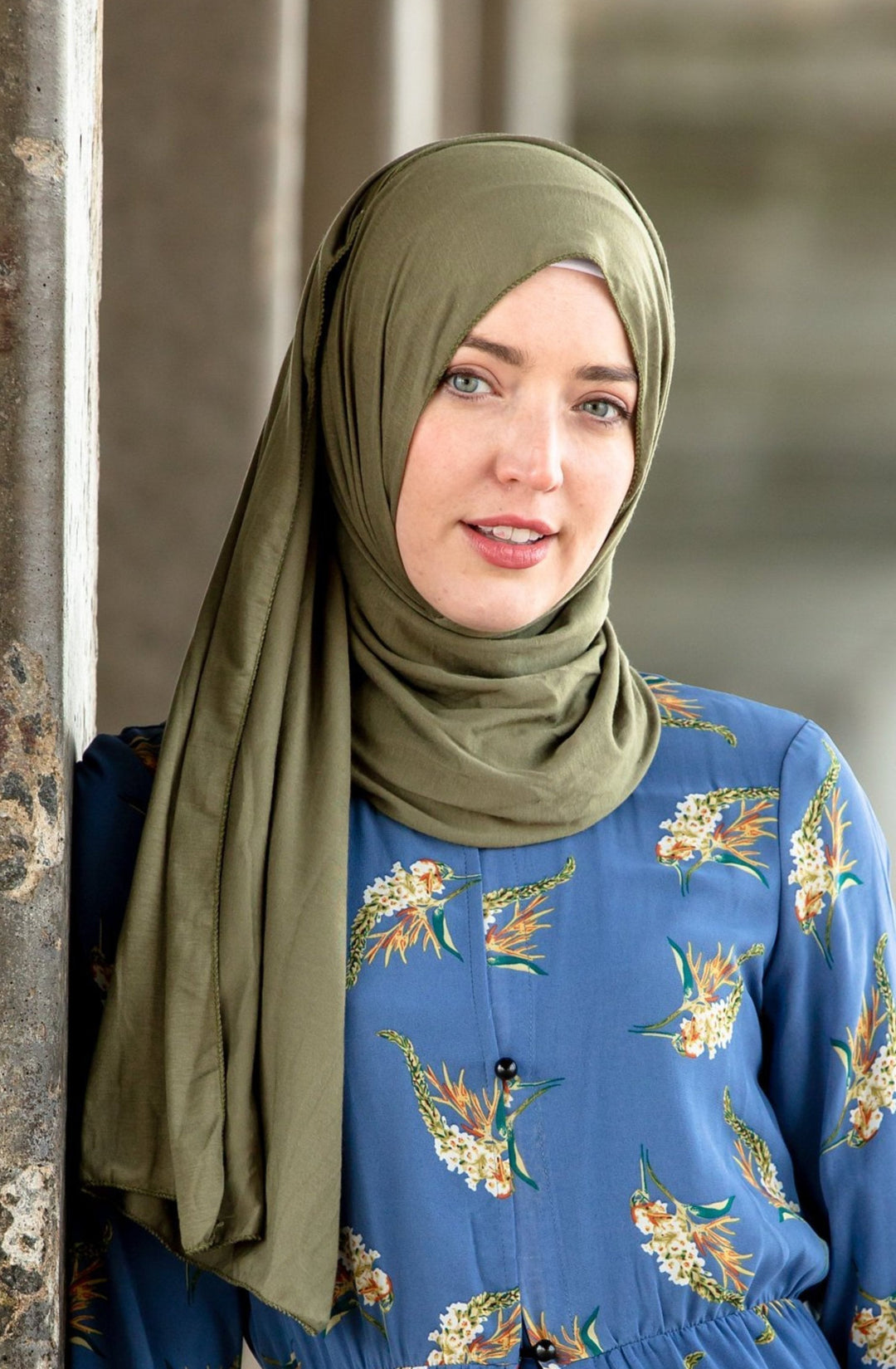 Woman in a green hijab and blue floral dress showcasing Olive Green Jersey Hijab