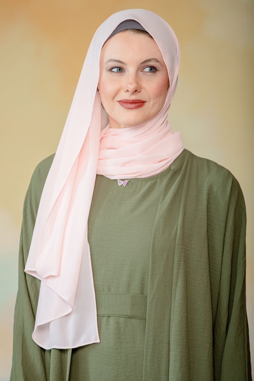 Woman in pink hijab and olive green dress showcasing a Peach Chiffon Hijab scarf