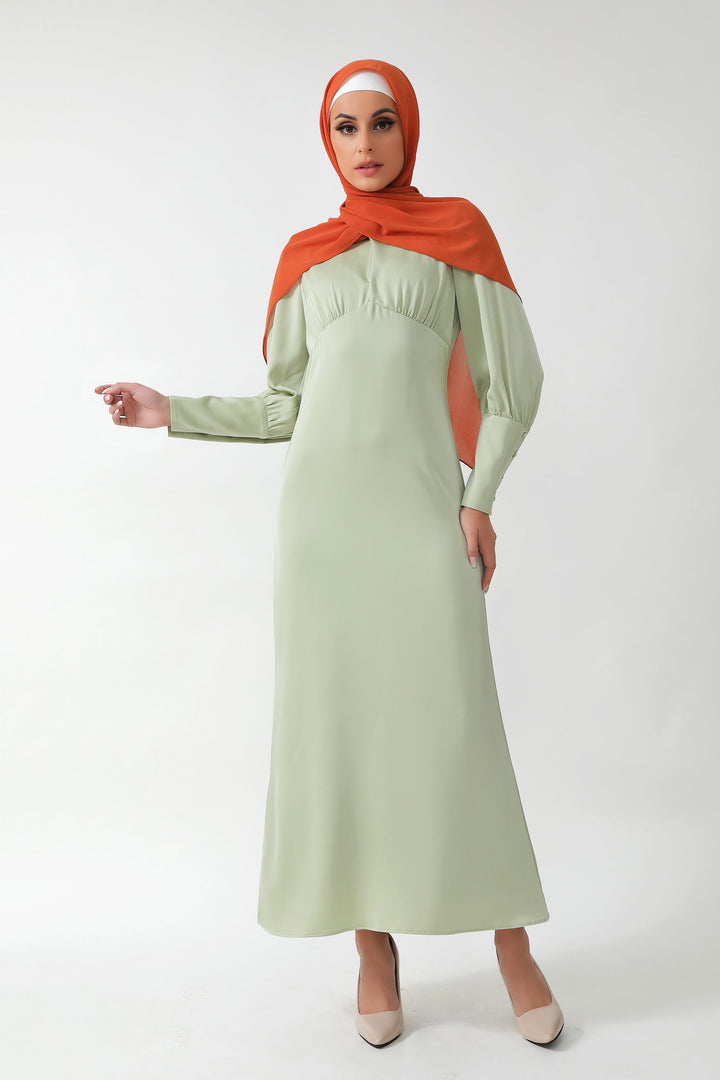 Woman wearing Pistachio Satin Long Sleeve Maxi Dress with batwing sleeves and orange hijab