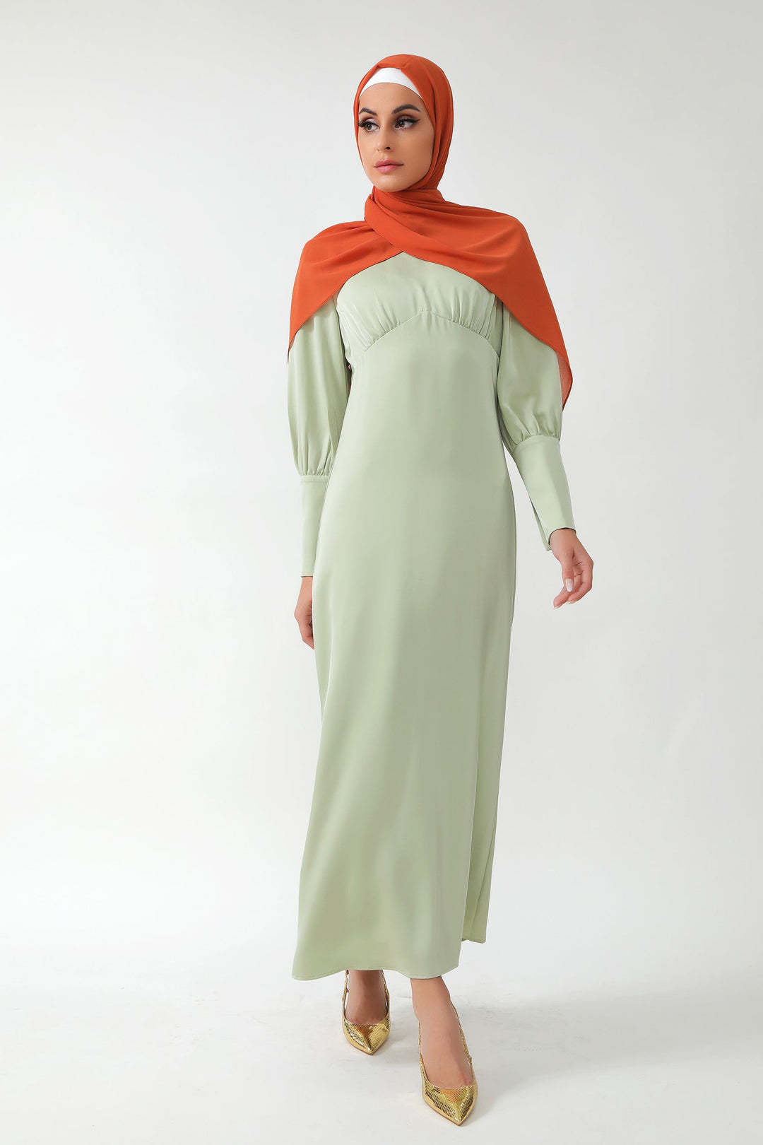 Woman in a modest pistachio satin long sleeve maxi dress with batwing sleeves and orange hijab