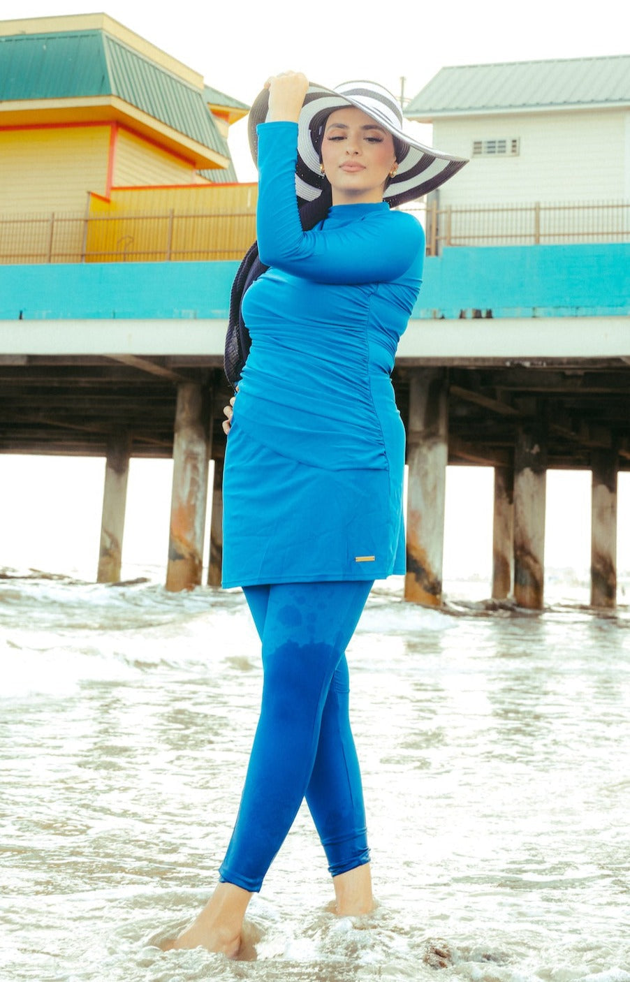 Blue modest swimsuit with ruched design and striped hat, perfect for sunny days