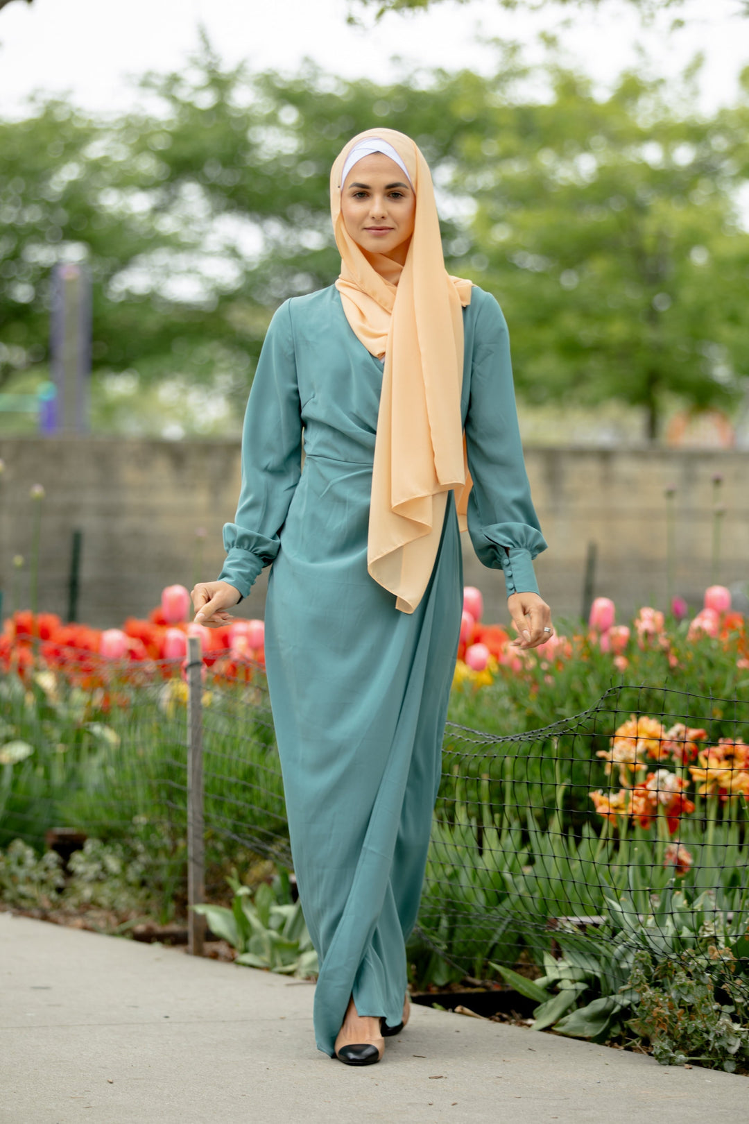 Woman in teal dress and peach hijab modeling a Sea Blue Wrap Maxi Dress with criss cross neckline