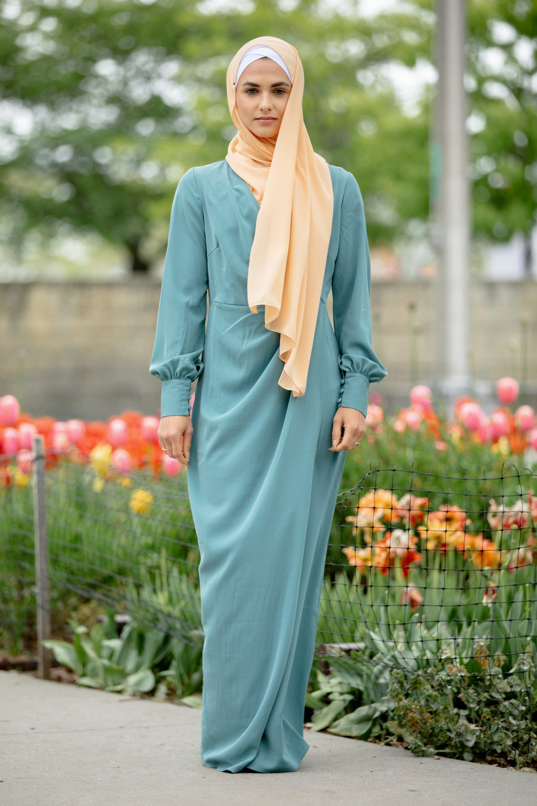 Woman in teal dress and peach hijab showcasing Sea Blue Wrap Maxi Dress with criss cross neckline