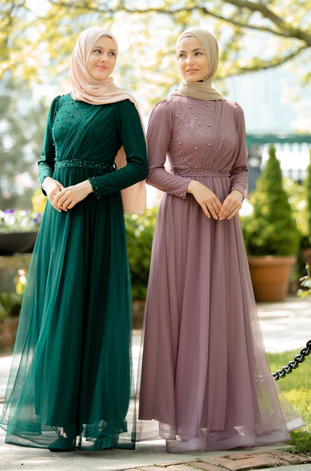 Two women in elegant, long-sleeved maxi dresses and hijabs featuring a pearl gown design