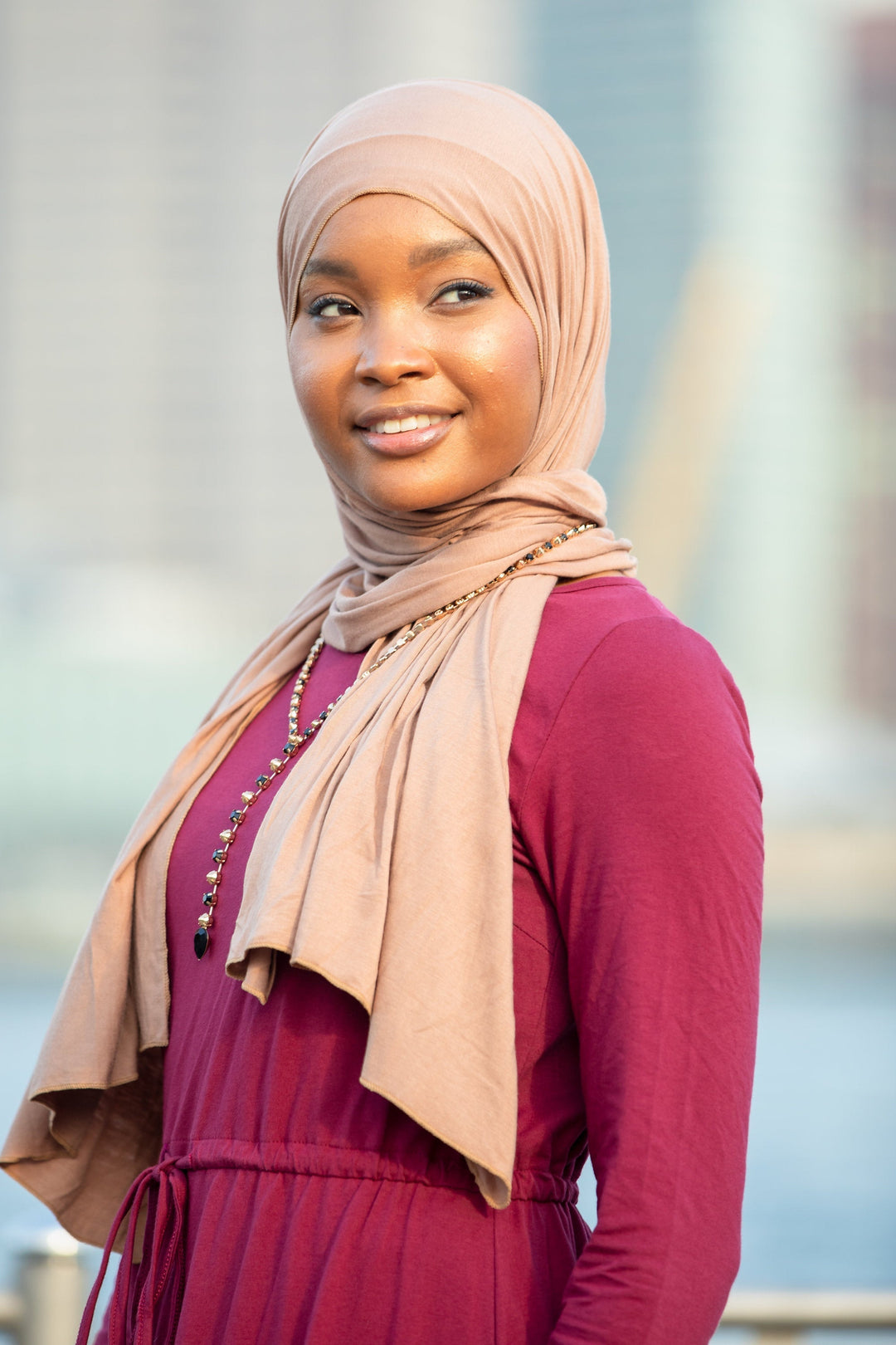 Woman in hijab and maroon dress showcasing a stylish jersey hijab in taupe