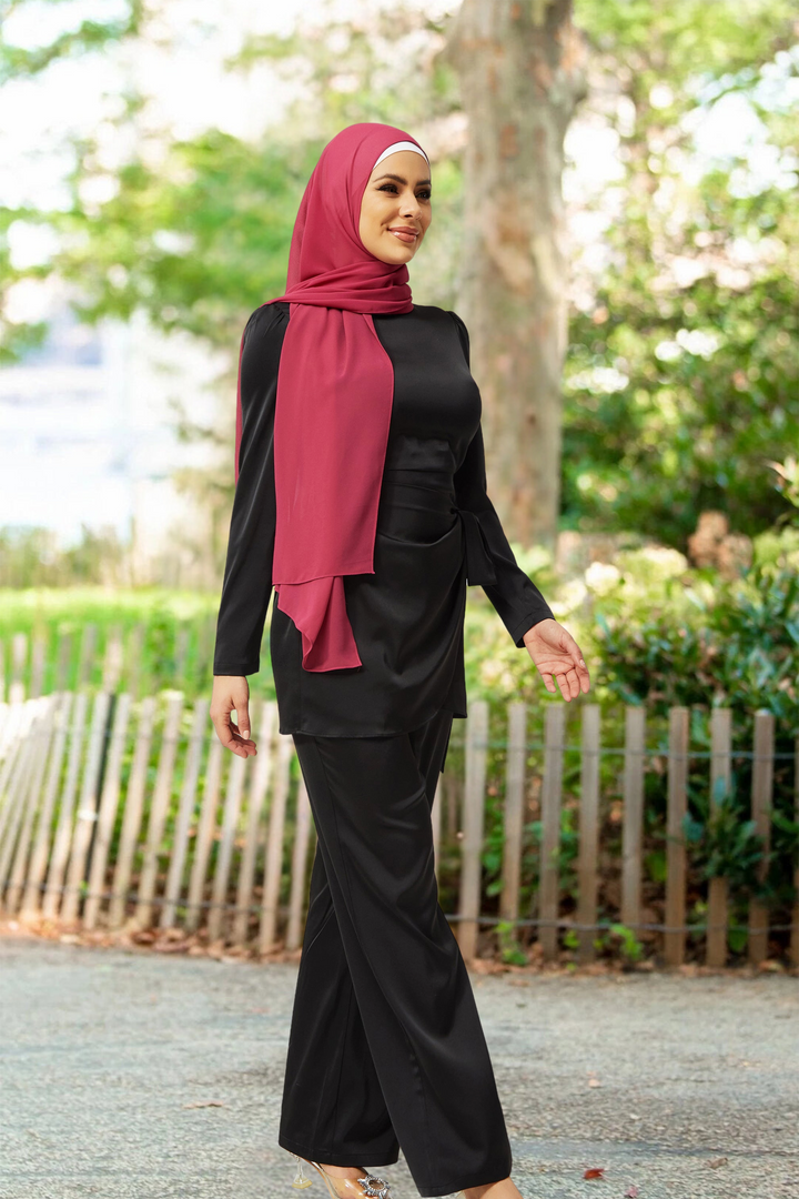 Woman in black satin side wrap tunic and pant set with red hijab