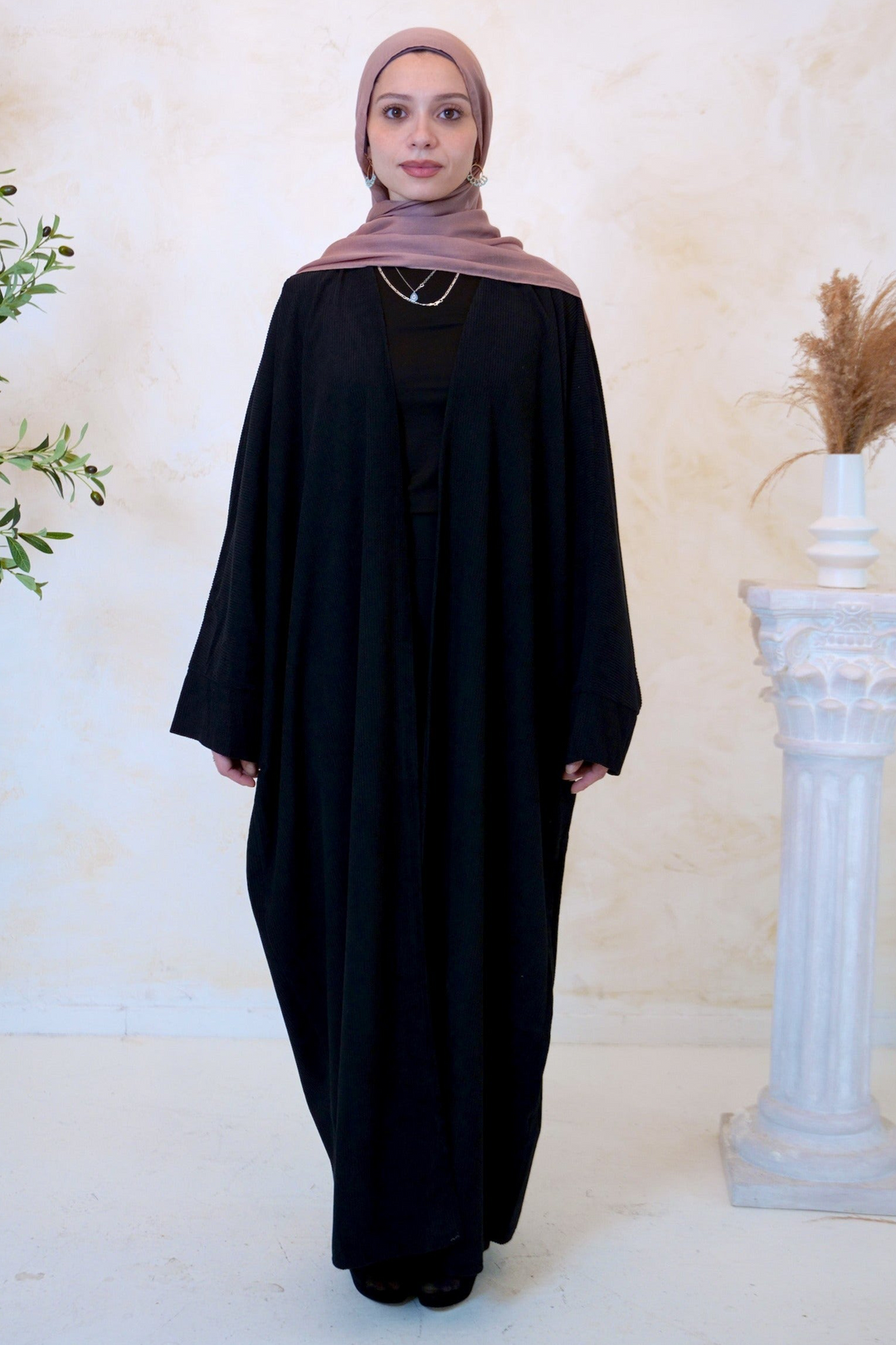 a woman in a black dress standing next to a vase