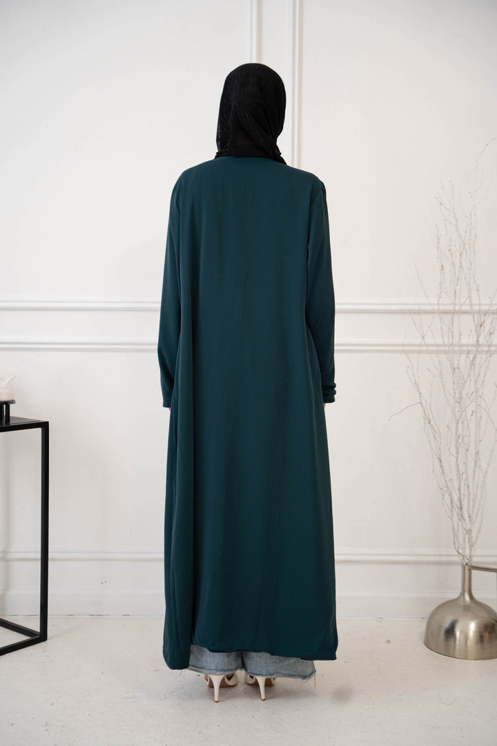 a woman standing in a room wearing a green coat