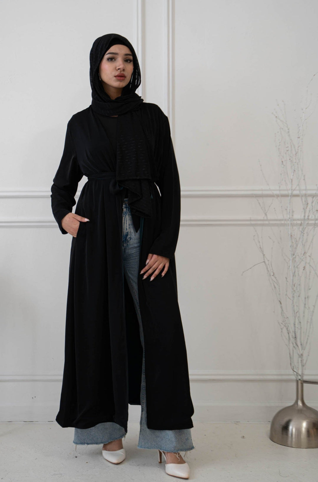 a woman standing in a room wearing a long black coat