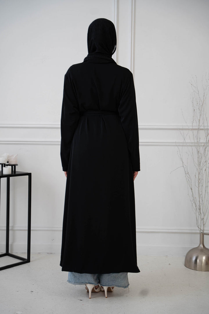 a woman in a long black coat standing in front of a white wall