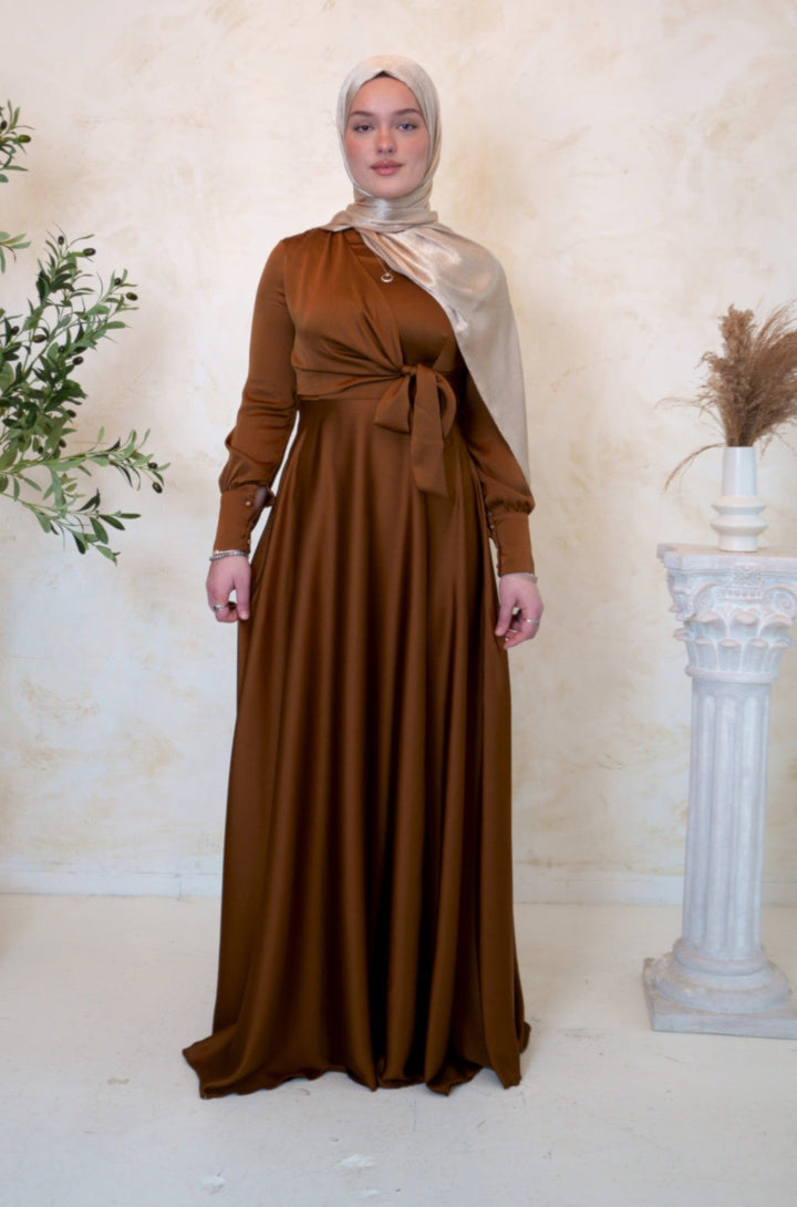 a woman in a brown dress standing next to a plant