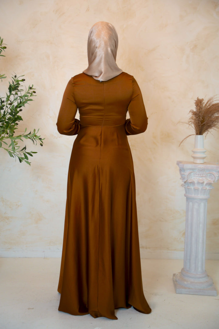 a woman in a brown dress standing next to a vase