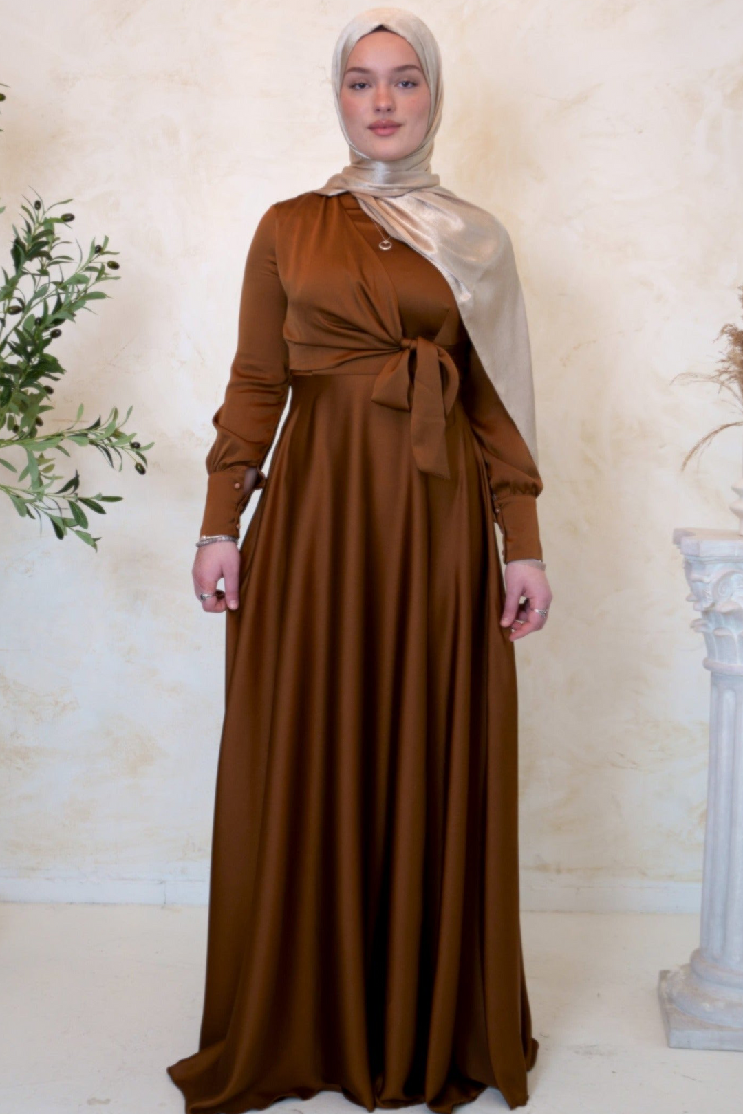 a woman in a brown dress standing next to a plant