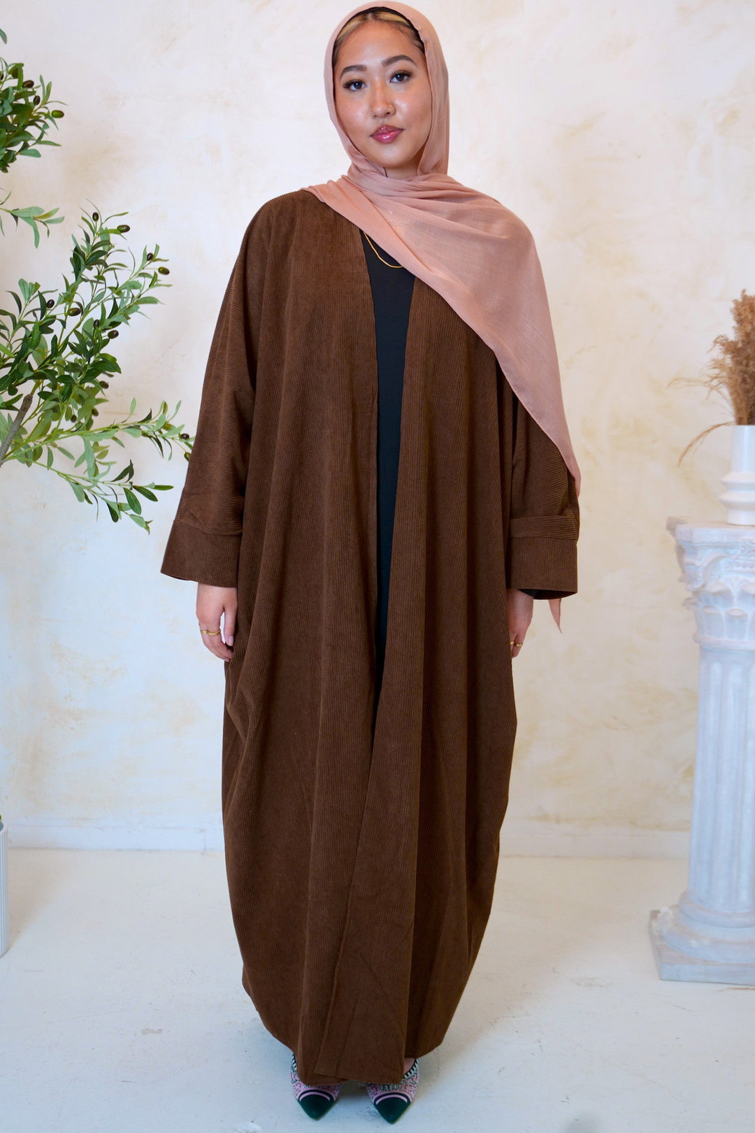 a woman in a brown robe standing in front of a plant