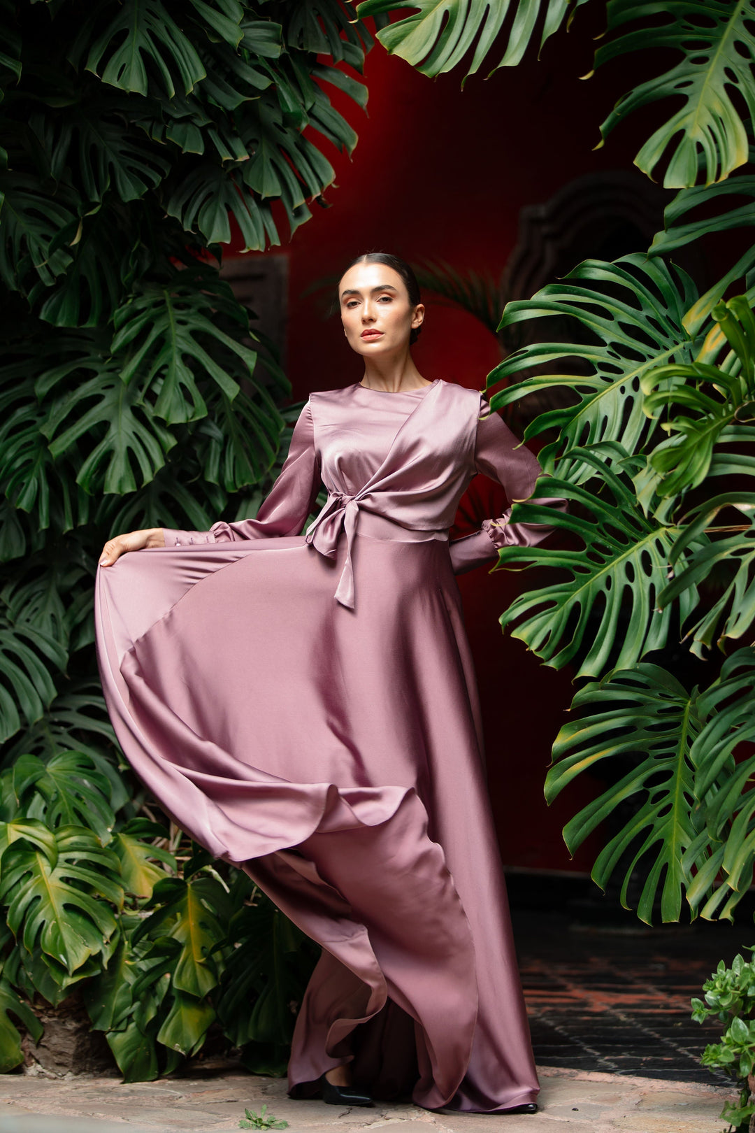 a woman in a long dress standing in front of a plant