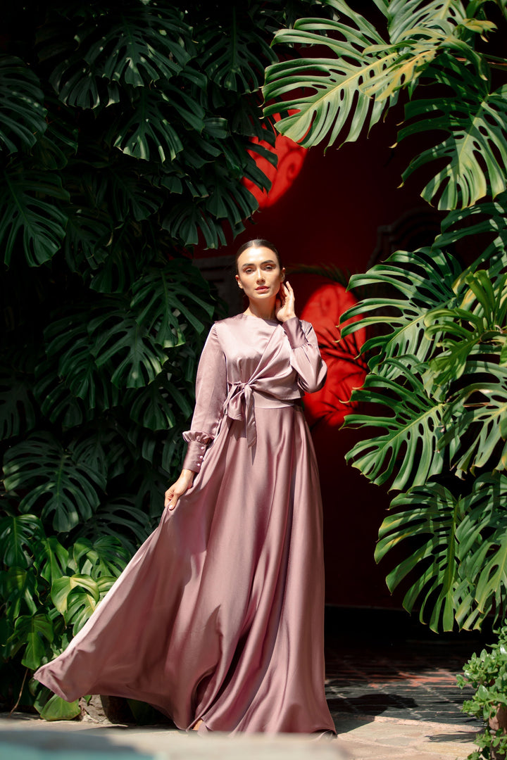 a woman in a long dress standing in front of a plant