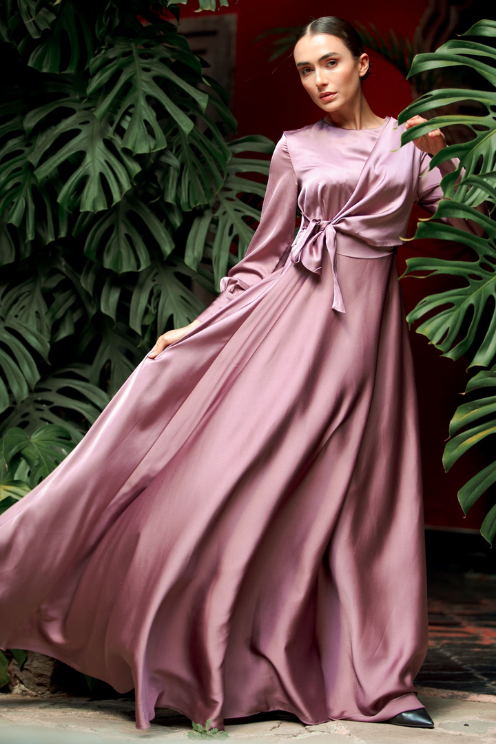 a woman in a long dress standing in front of a plant