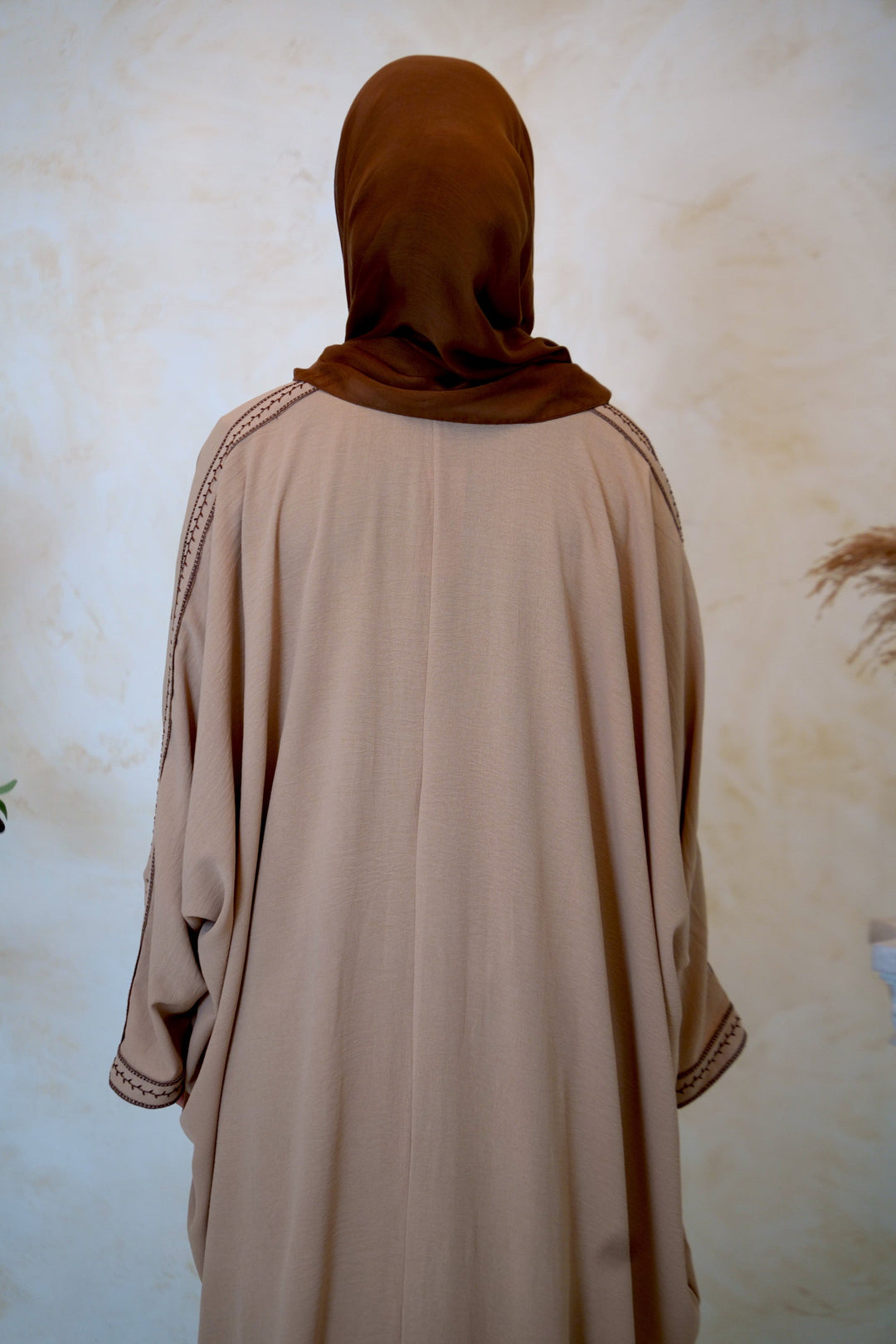 a woman wearing a brown shawl standing in front of a wall