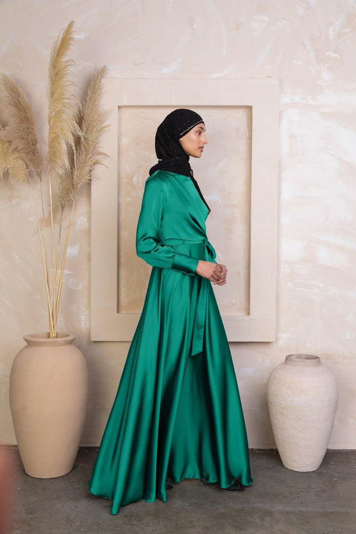 a woman in a green dress standing next to a vase