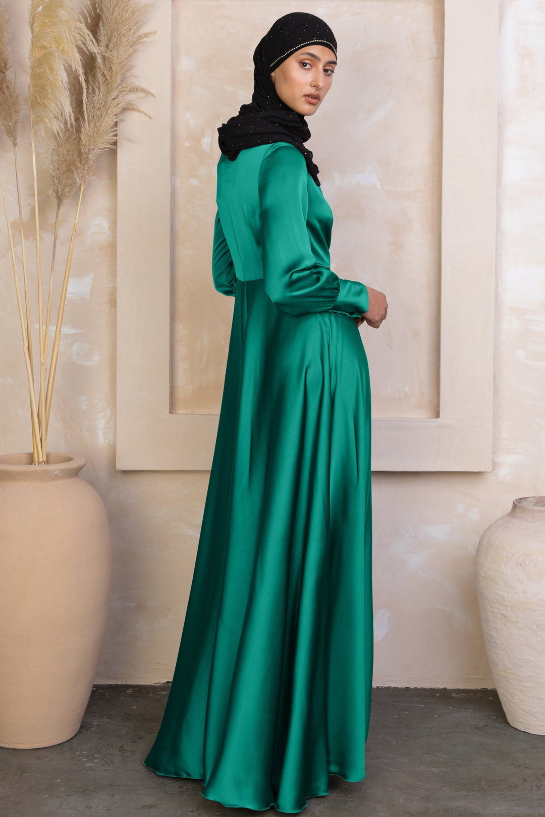 a woman in a green dress standing next to a vase