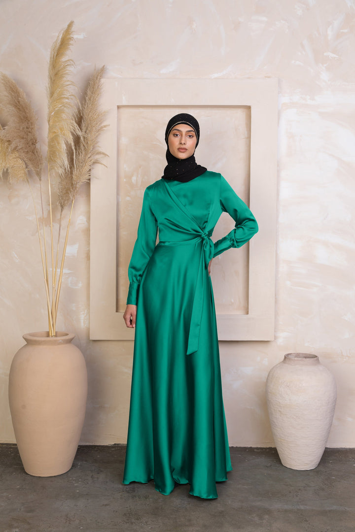 a woman in a green dress standing next to a vase