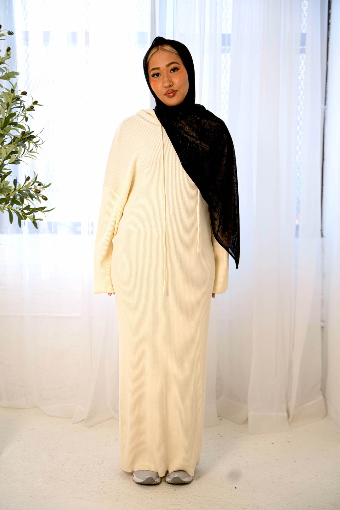 a woman standing in front of a window wearing a white dress and black shawl
