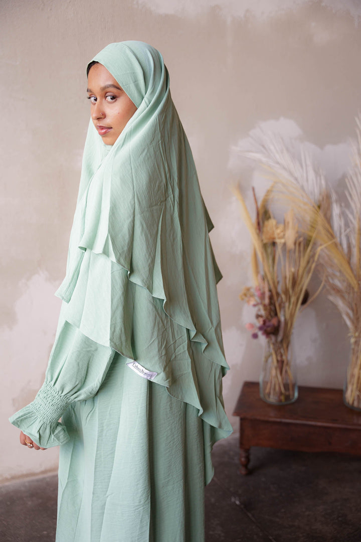 a woman wearing a green hijab standing in front of a wall