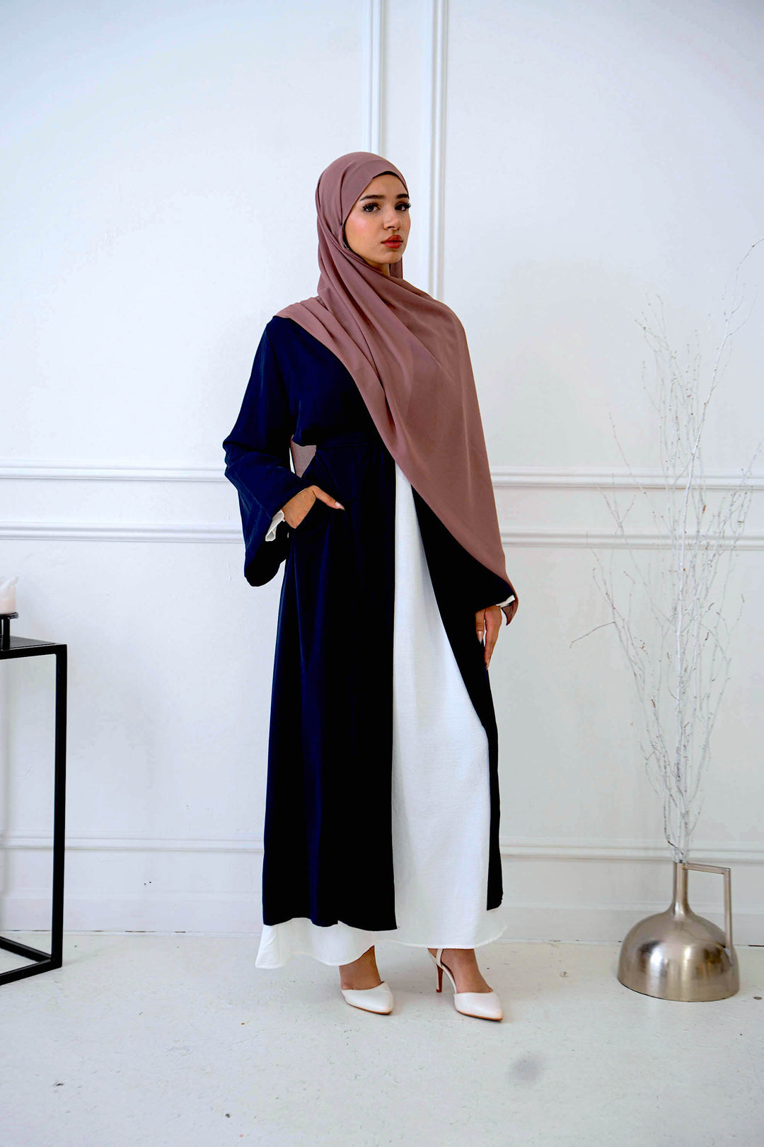 a woman wearing a hijab standing in front of a white wall