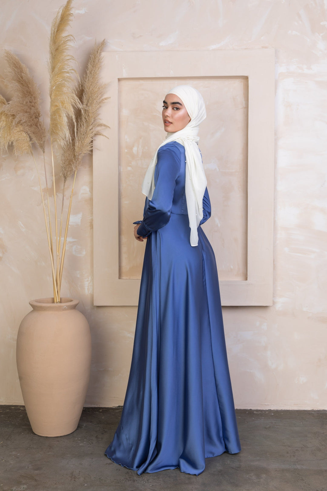 a woman in a blue dress standing next to a vase