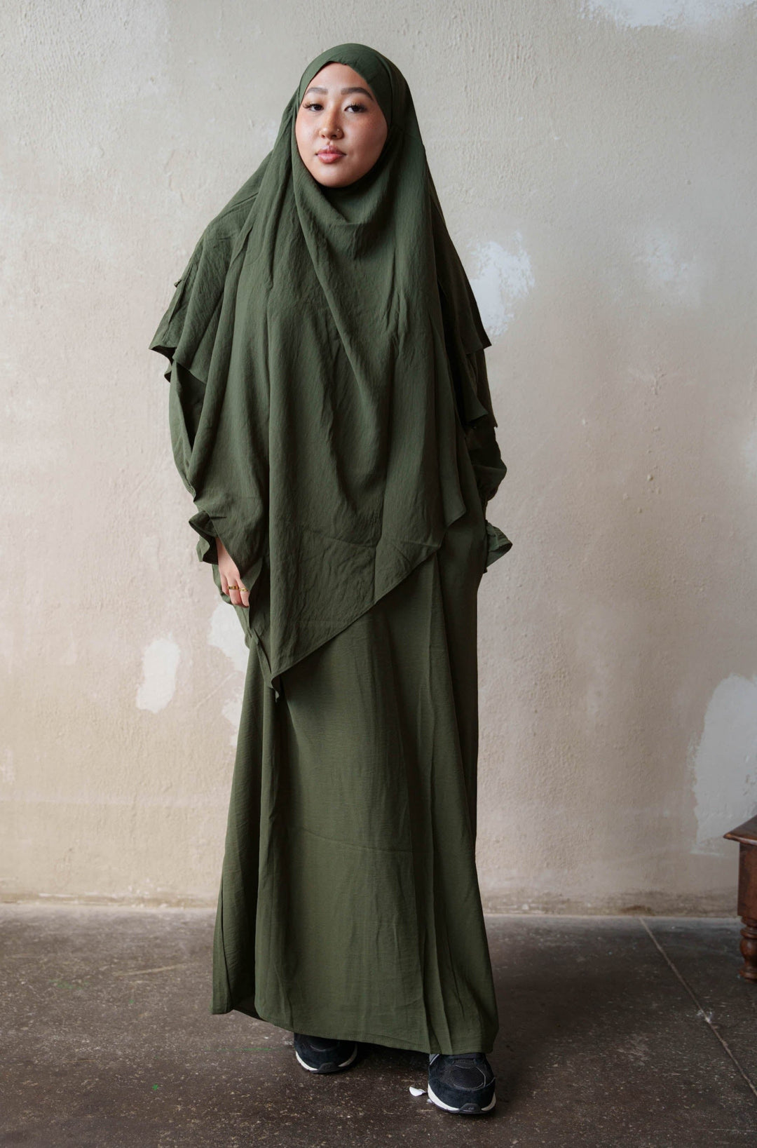 a woman wearing a green hijab standing in front of a wall