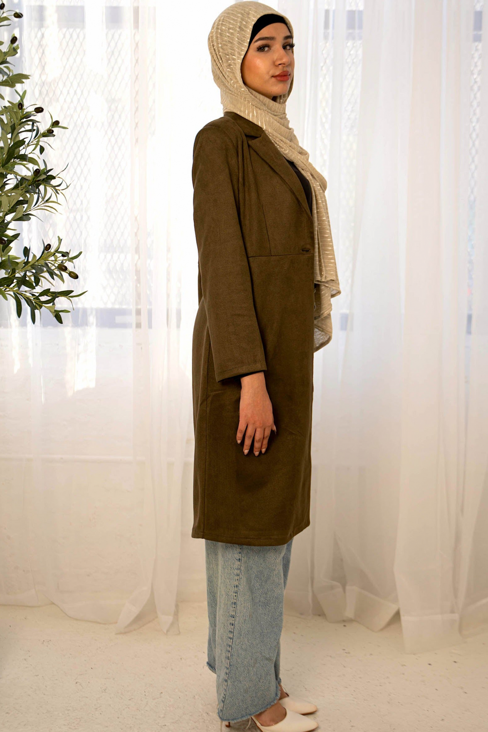 a woman standing in front of a window wearing a brown coat