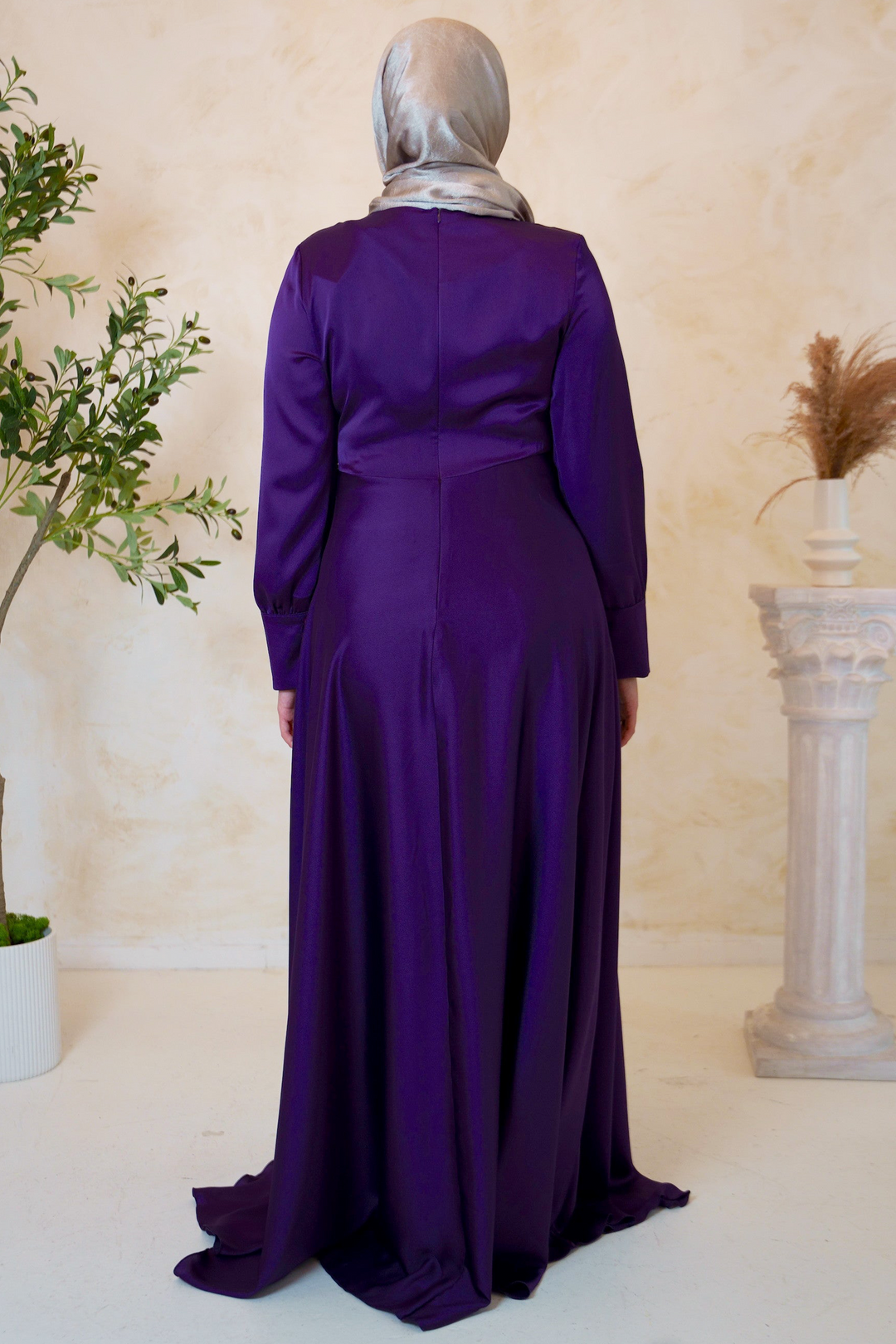 a woman in a purple dress standing in front of a plant